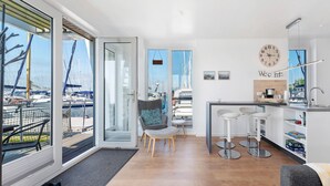 A modern kitchen with a view of boats, a dining area with bar stools, and a large window. - Houseboat 'Sutje' with Sea View, Private Terrace and Wi-Fi (Großenbrode)