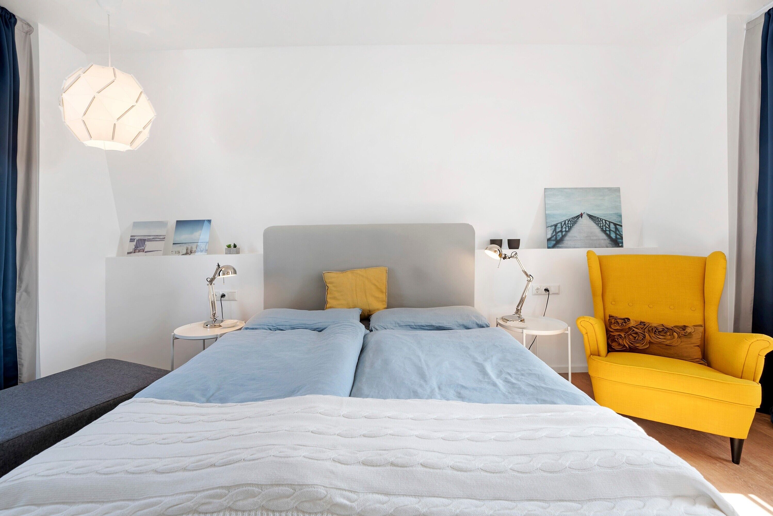 A modern bedroom with a bed, bedside tables, a chair, and a pendant light.