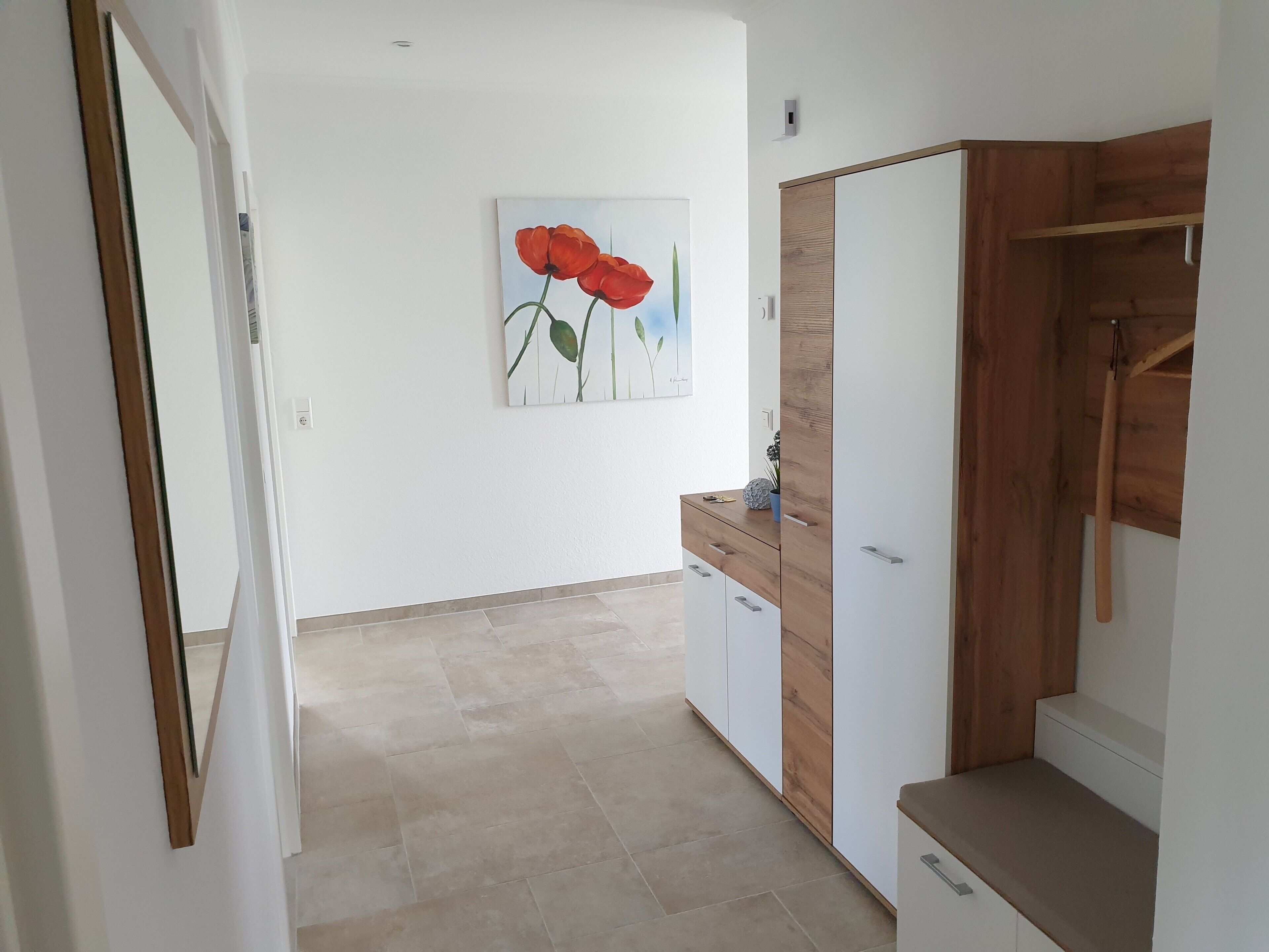 A hallway with a wooden wardrobe, a small cabinet, and a painting of red flowers on the wall.