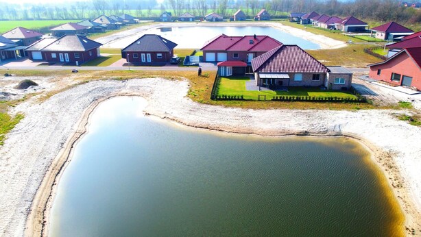An aerial view of a residential area with houses, a large pond, and a grassy field.