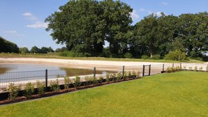 A grassy area with a fence, trees, and a body of water.