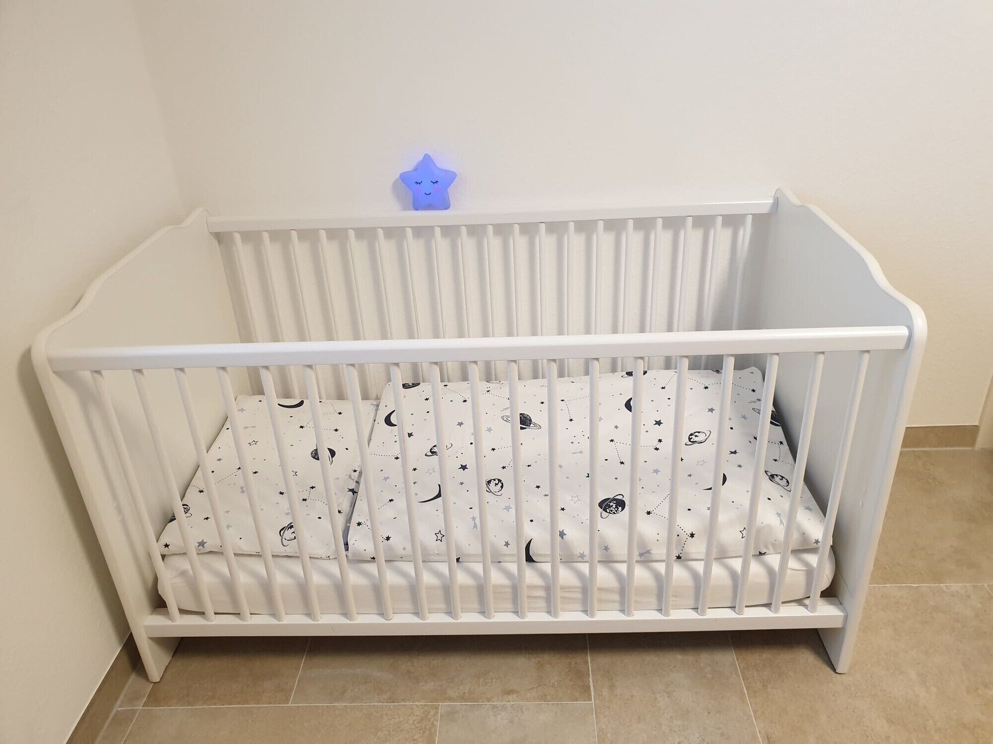 Un berceau blanc avec un matelas orné de motifs en forme d’étoiles, une veilleuse bleue en forme d’étoile et un mur uni.