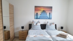 A bedroom with a bed, two bedside tables, a nightstand, a mirror, and a painting of a sunset over a pier.