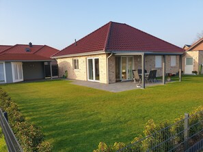 Une maison d’habitation dotée d’un patio couvert, d’une pelouse et d’une façade en briques.