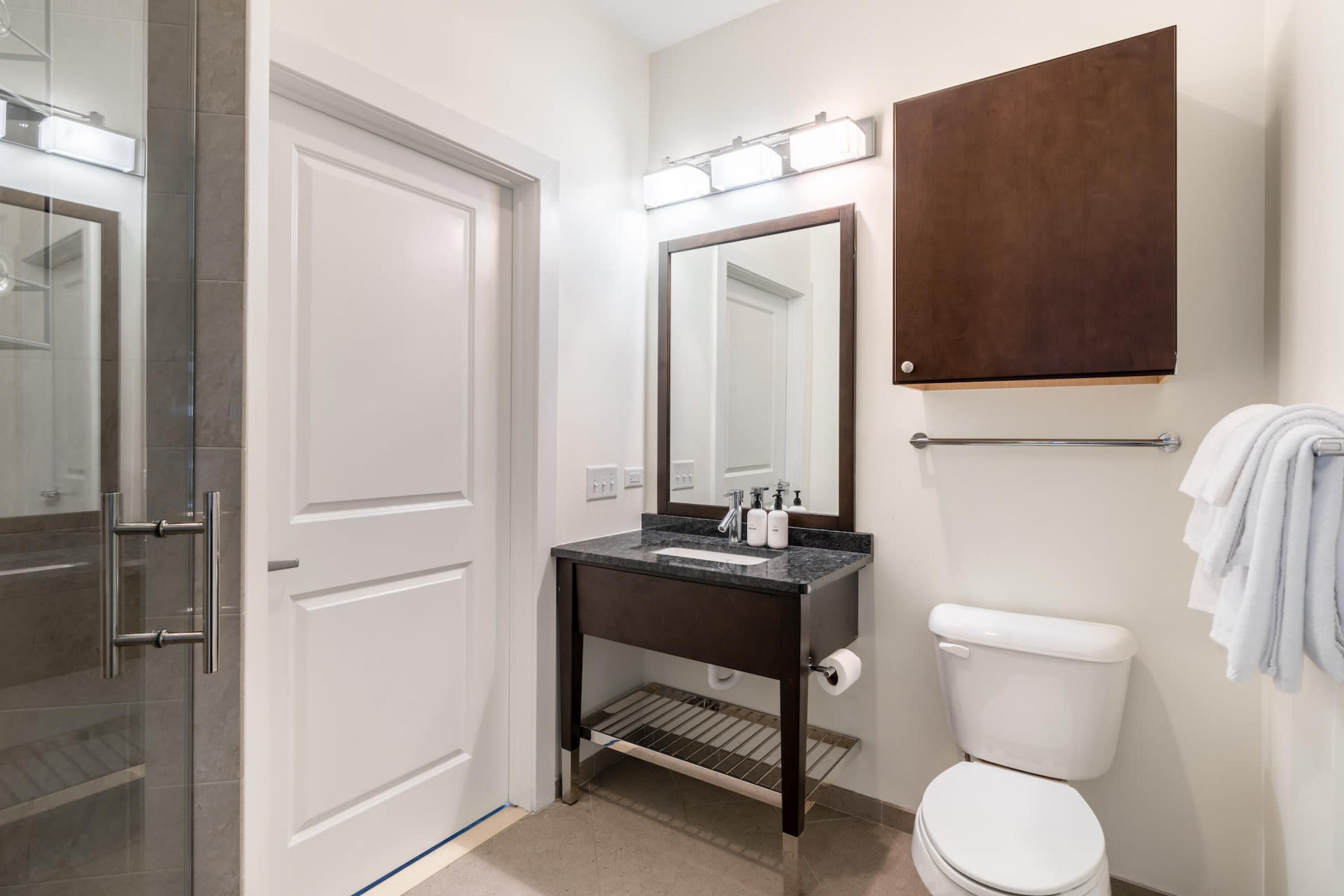 A modern bathroom with a glass shower enclosure, a dark countertop sink, a large mirror, and a white toilet.