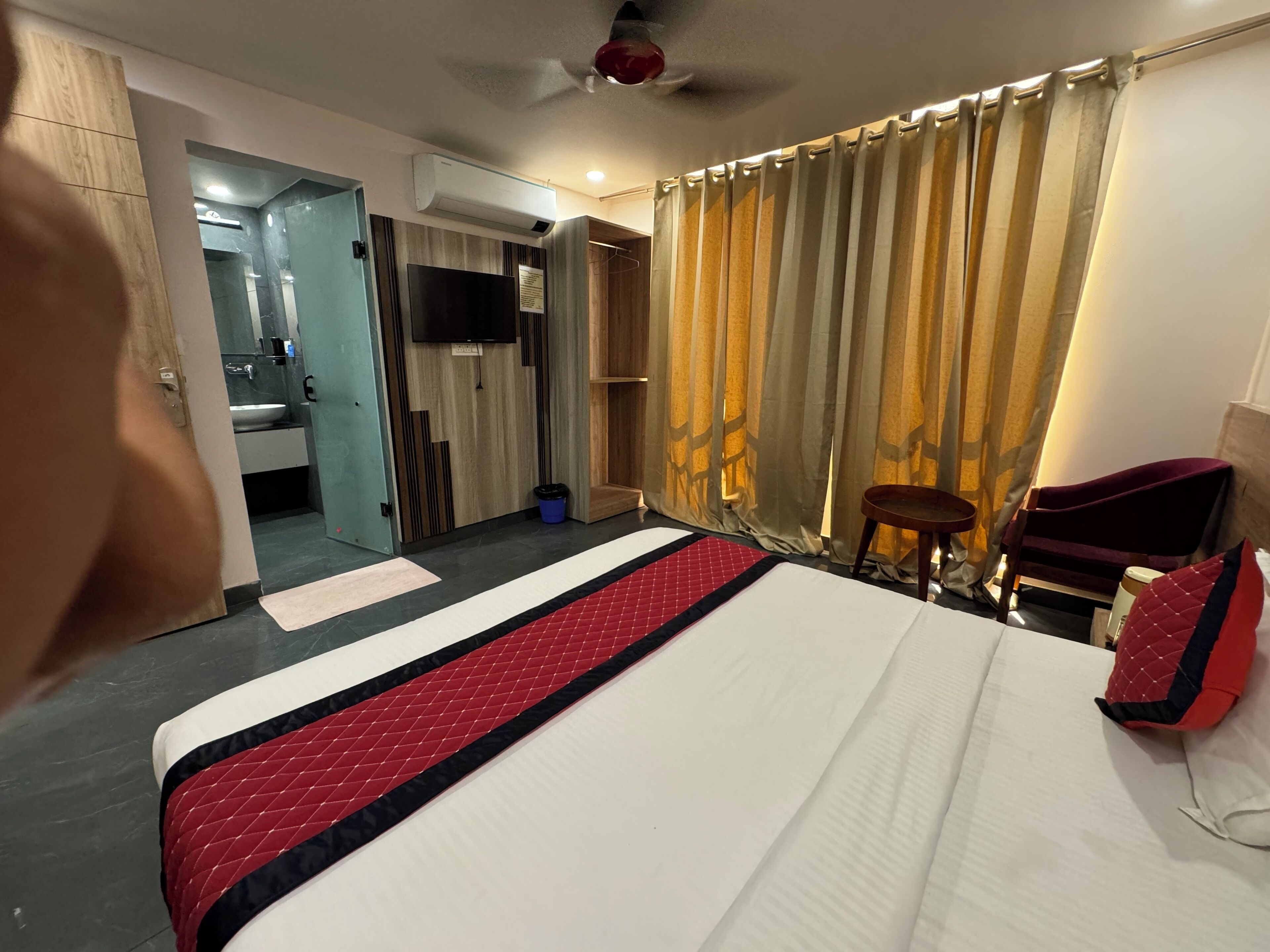 Habitación de hotel con cama, televisor, ventilador de techo y baño visible a través de una puerta abierta.