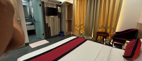 Habitación de hotel con cama, televisor, ventilador de techo y baño visible a través de una puerta abierta.