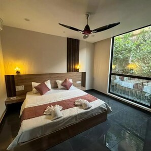 A hotel room with a large bed, a ceiling fan, and a balcony with a view of greenery. - Namay Inn By T And M Hotels (Haridwar)