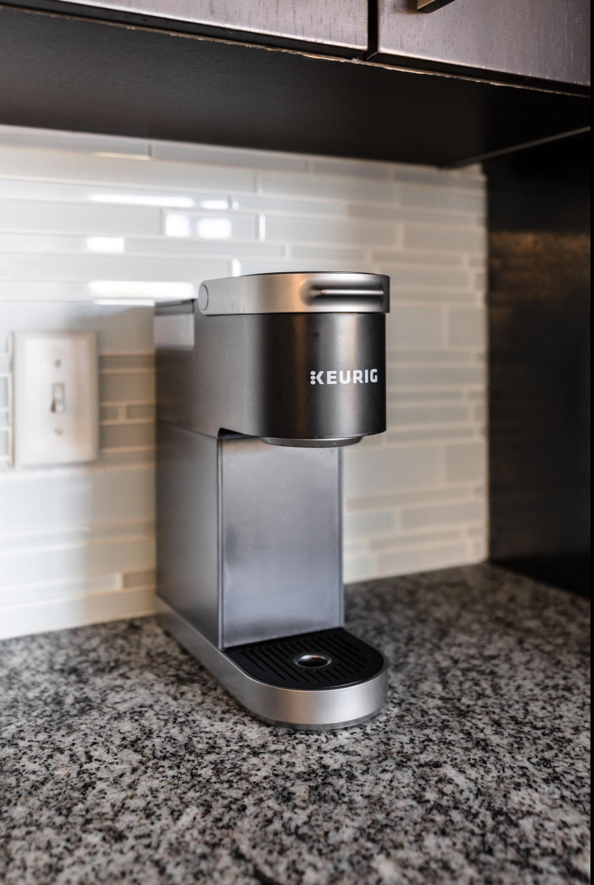Una cafetera moderna y elegante con acabado metálico, ubicada sobre una encimera de granito en una cocina.