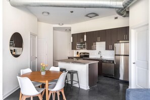 A modern kitchen with dark cabinets, stainless steel appliances, and a central island. - Kasa Comfy 2 BD Gym Access Alexandria (Alexandria)