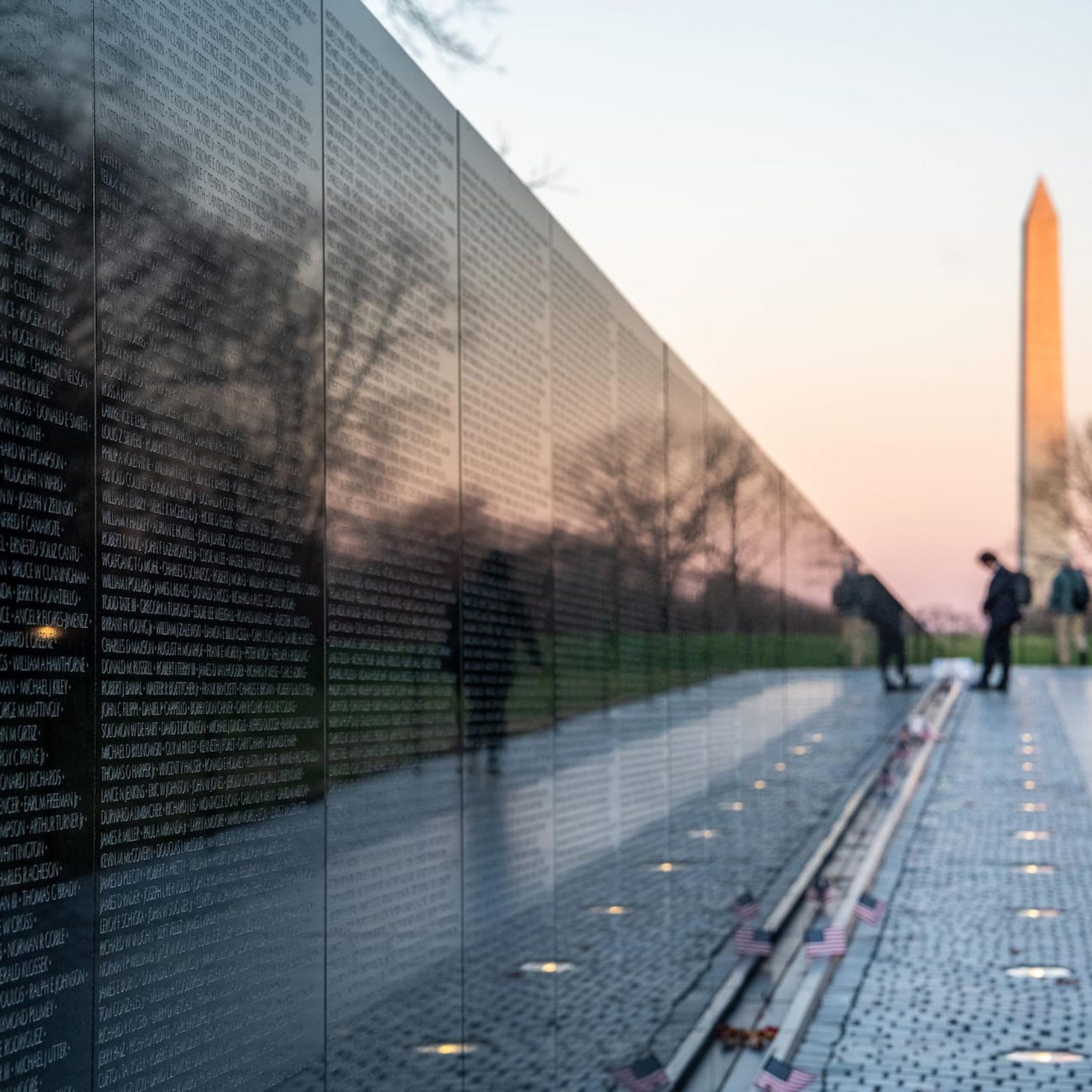 A memorial wall with engraved names, a clear sky, and a distant monument.