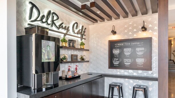 A modern coffee bar with a Starbucks refrigerator, a menu board, and two stools.