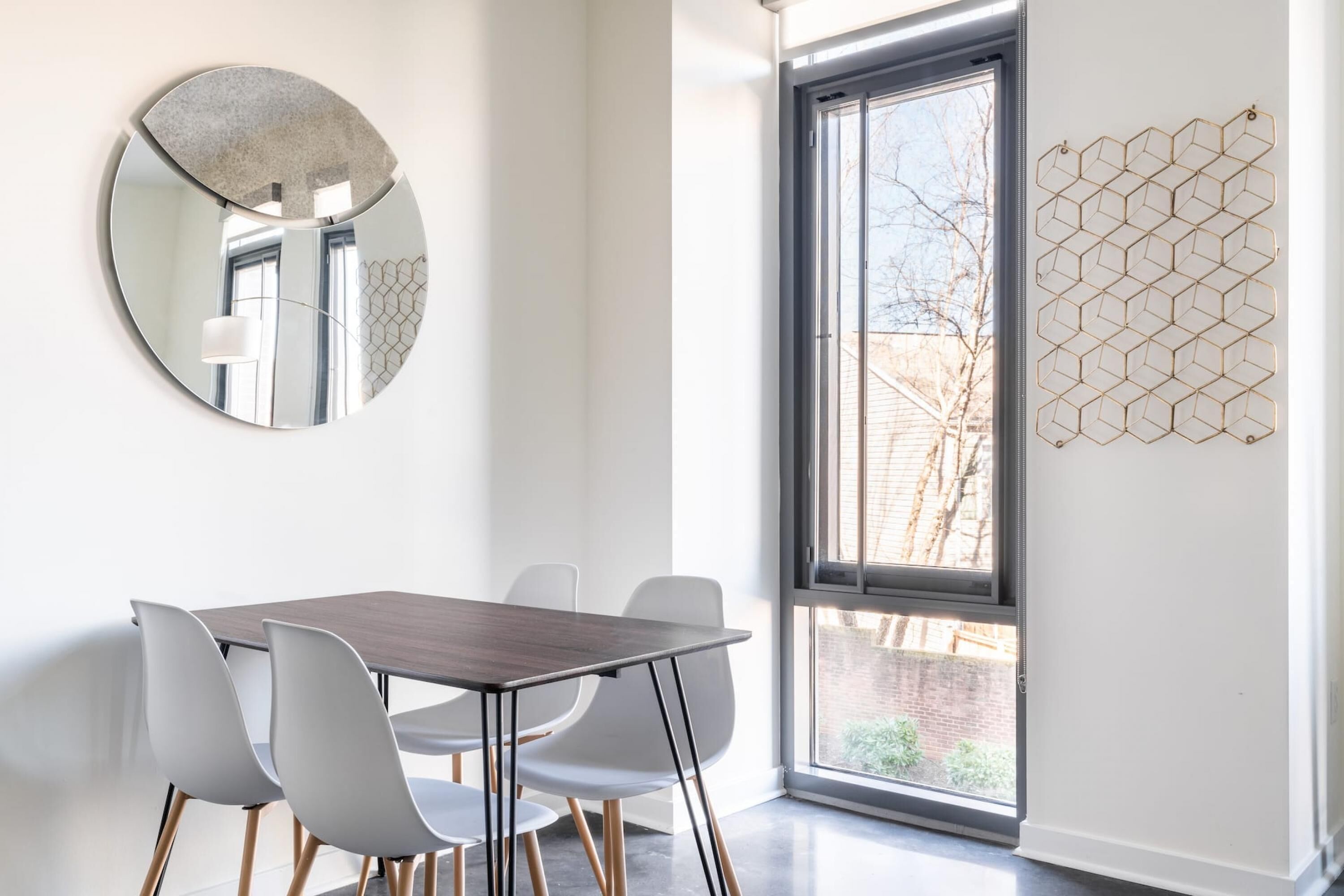 A dining area with a round mirror, a hexagonal wall decoration, and a view through a large window.