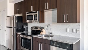 A modern kitchen with stainless steel appliances, dark wooden cabinets, and a granite countertop.