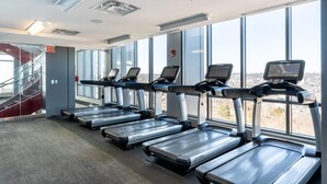 A gym with treadmills aligned against a wall with large windows, a staircase, and an exit sign. - Kasa Welcoming 1 BD Amenity Access Alexandria (Alexandria)