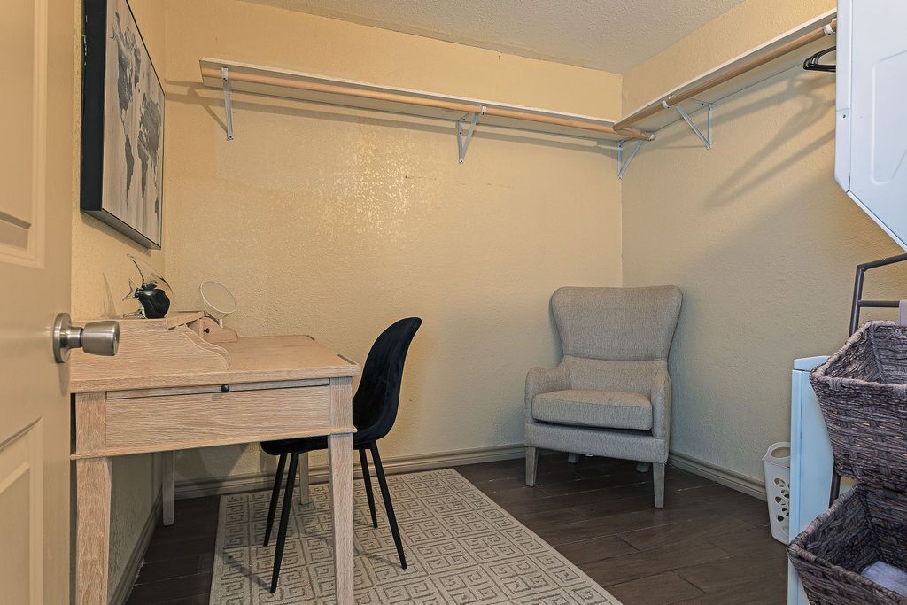 Een kleine kamer met een bureau, stoel en een grijze fauteuil.