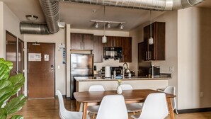 A modern kitchen with stainless steel appliances, a wooden dining table with white chairs, and a large green plant. - Kasa Family Friendly Westown 2BD Amenity Access Milwaukee (Milwaukee)