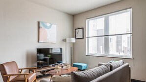 A modern living room with a sofa, armchair, TV, and a large window.