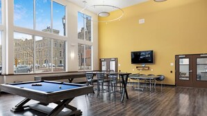 A pool table in a room with large windows, a television, and several chairs.