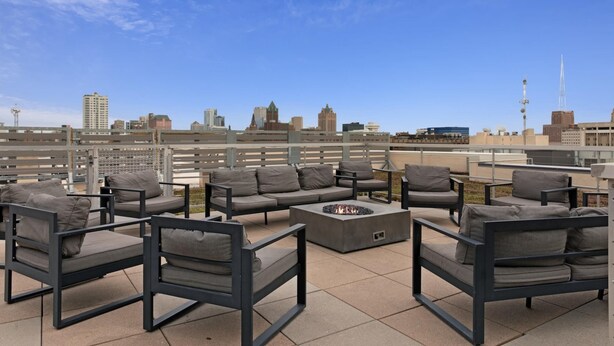 An outdoor seating area with modern furniture and a fire pit, overlooking a city skyline.