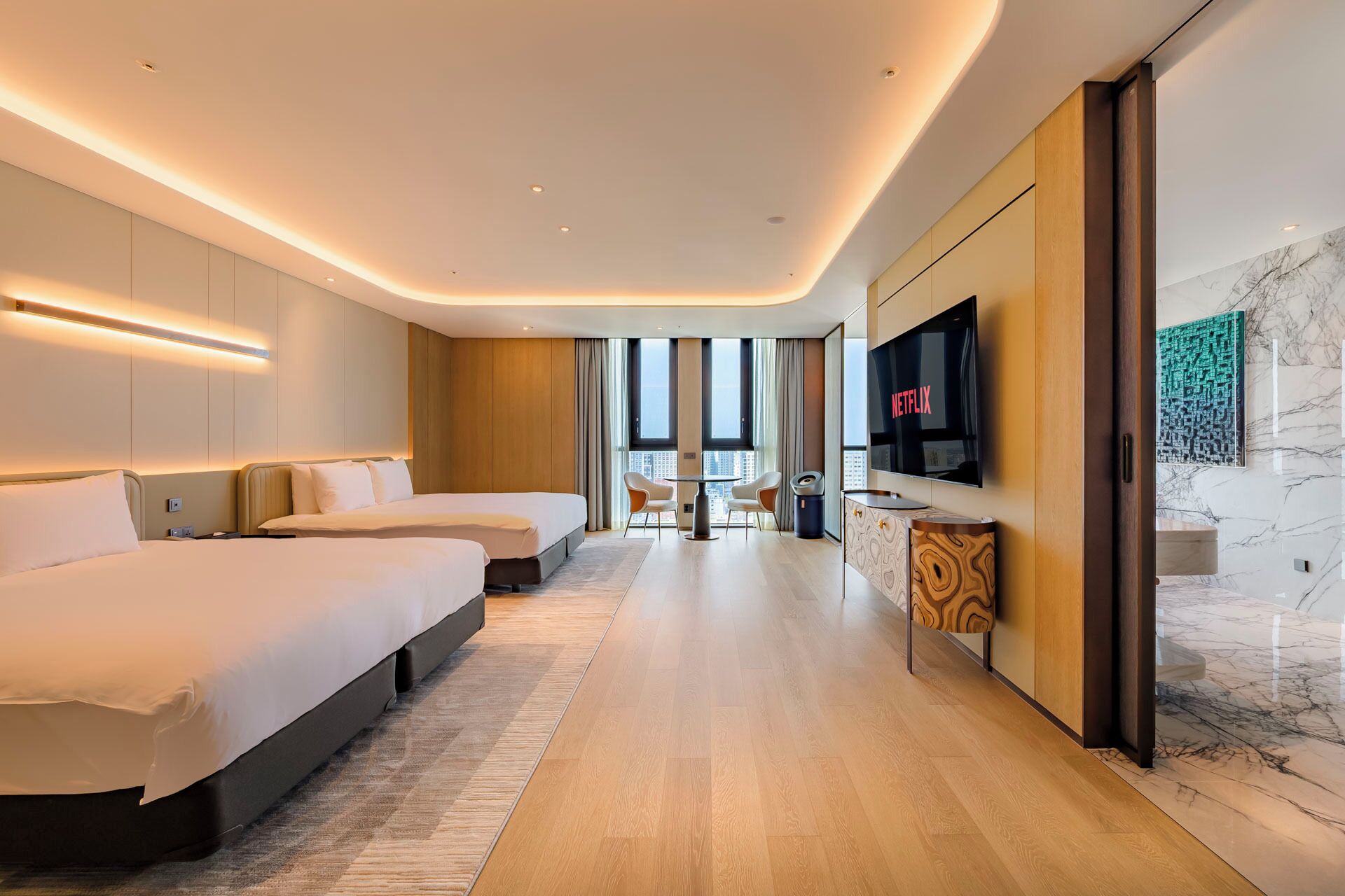 A modern hotel room with two beds, a TV, and a city view.