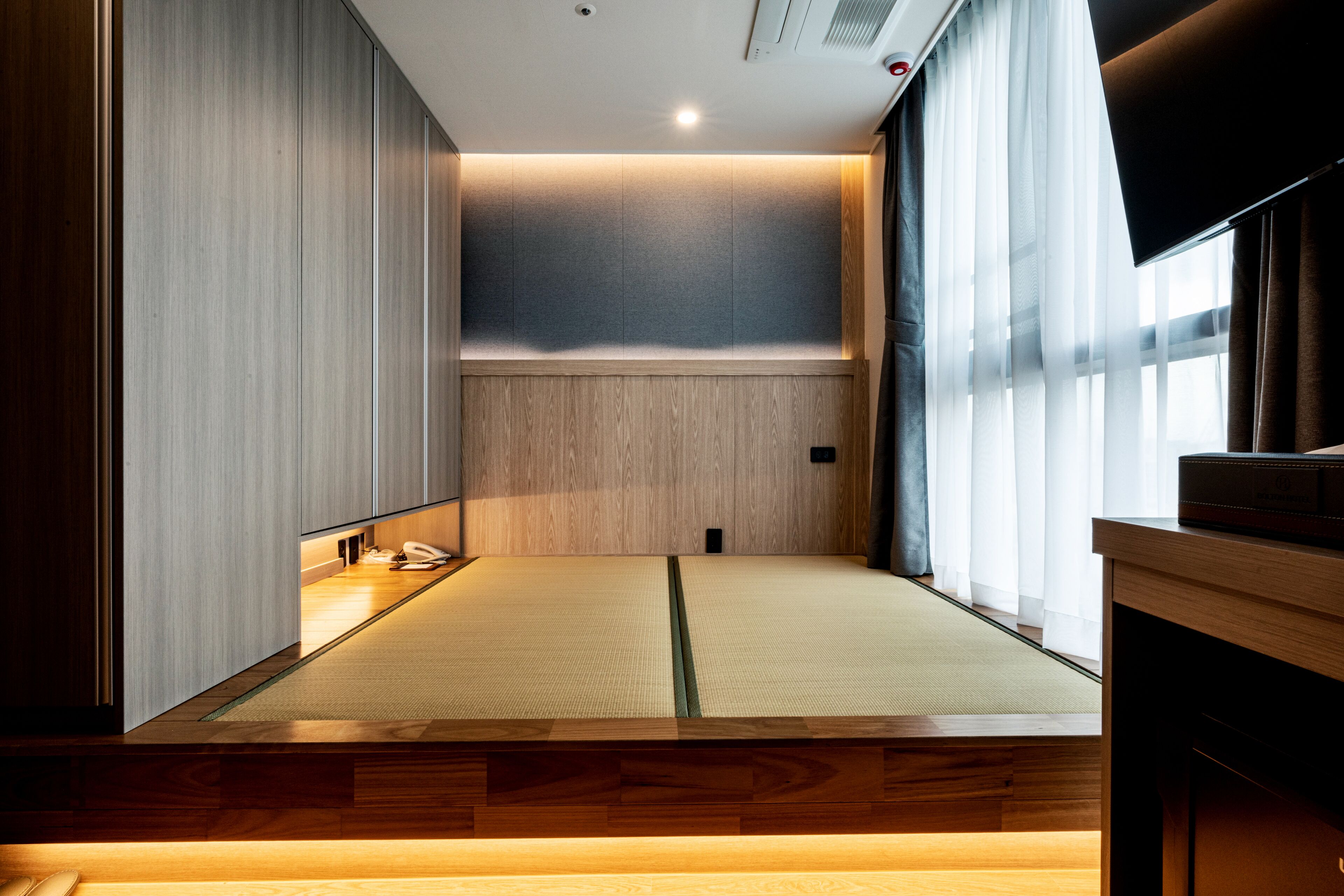 Una habitación japonesa tradicional con suelo de tatami, una cama de madera baja y puertas correderas.