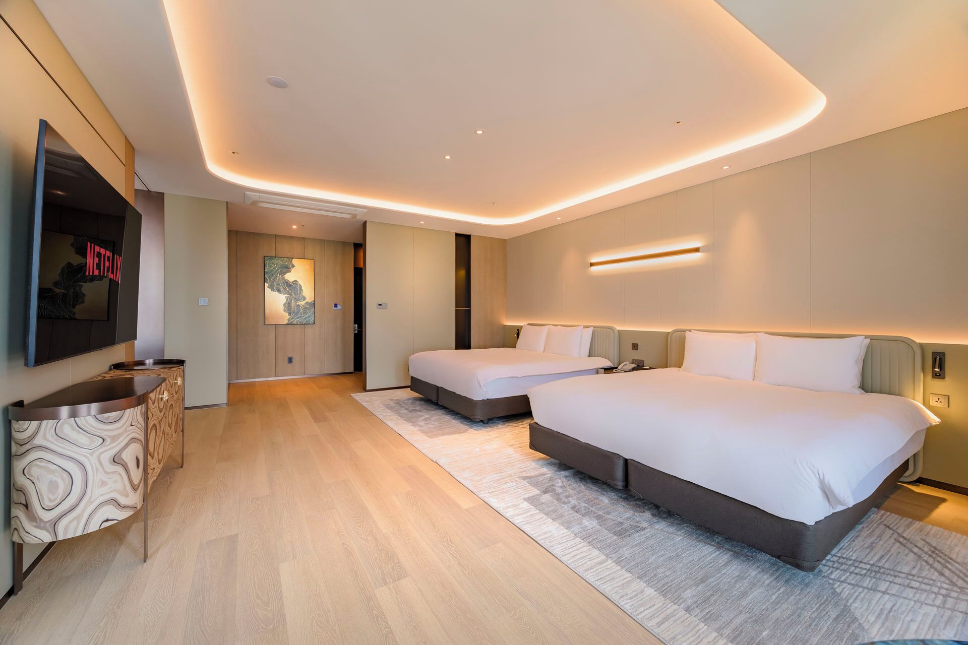 A modern hotel room with two beds, a flat-screen TV, and a wooden cabinet.