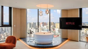 Ein modernes Zimmer mit einer großzügigen Badewanne, einem Flachbildfernseher und Blick auf die Stadt.