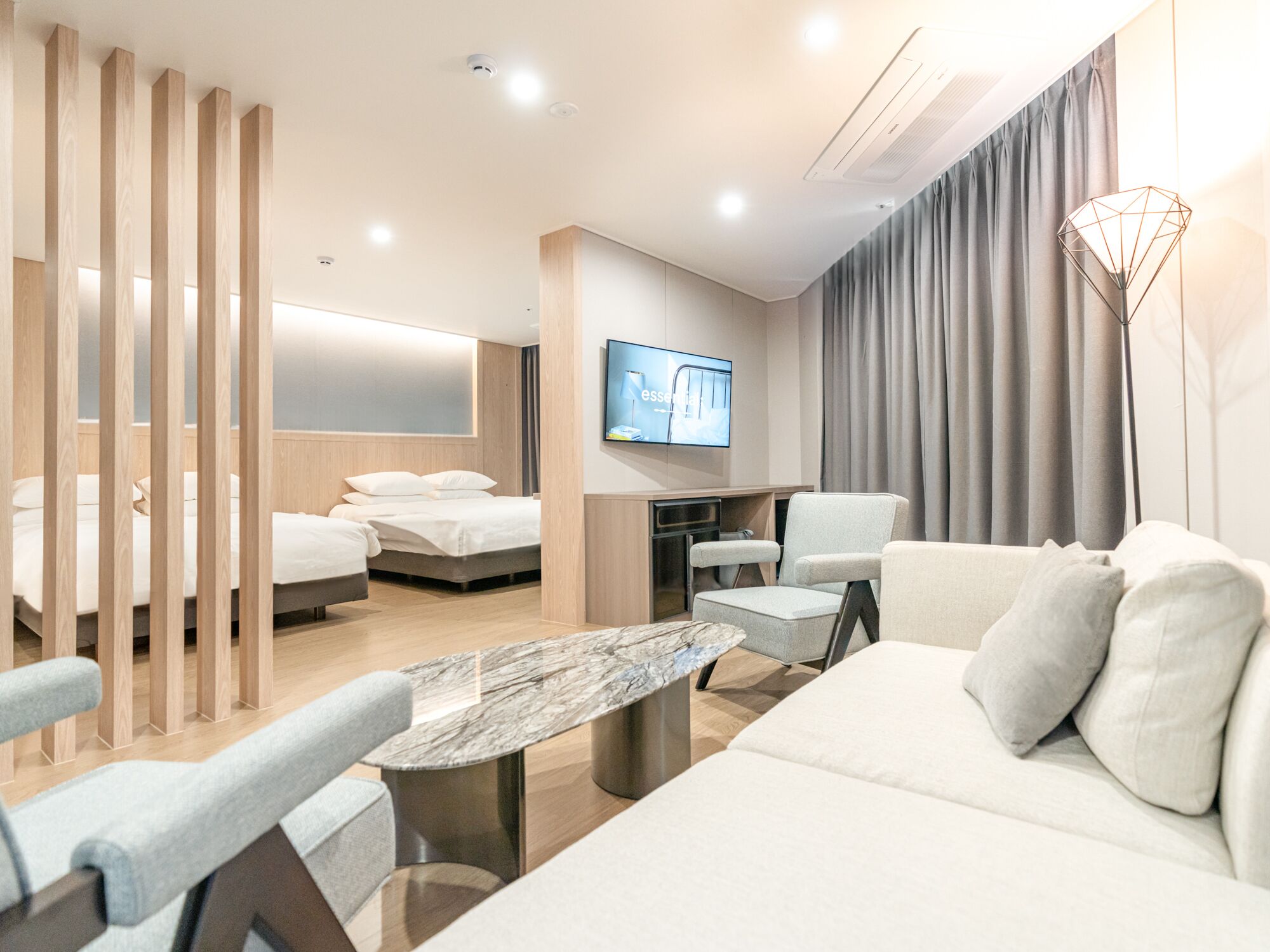A modern hotel room with a sofa, a dining table, a TV, and two beds.