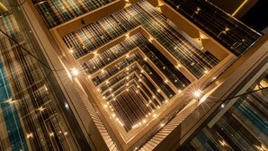 Ein Blick von oben in den Innenraum eines modernen Gebäudes, mit geometrischen Mustern an Wänden und Decke sowie mehreren Balkonebenen.