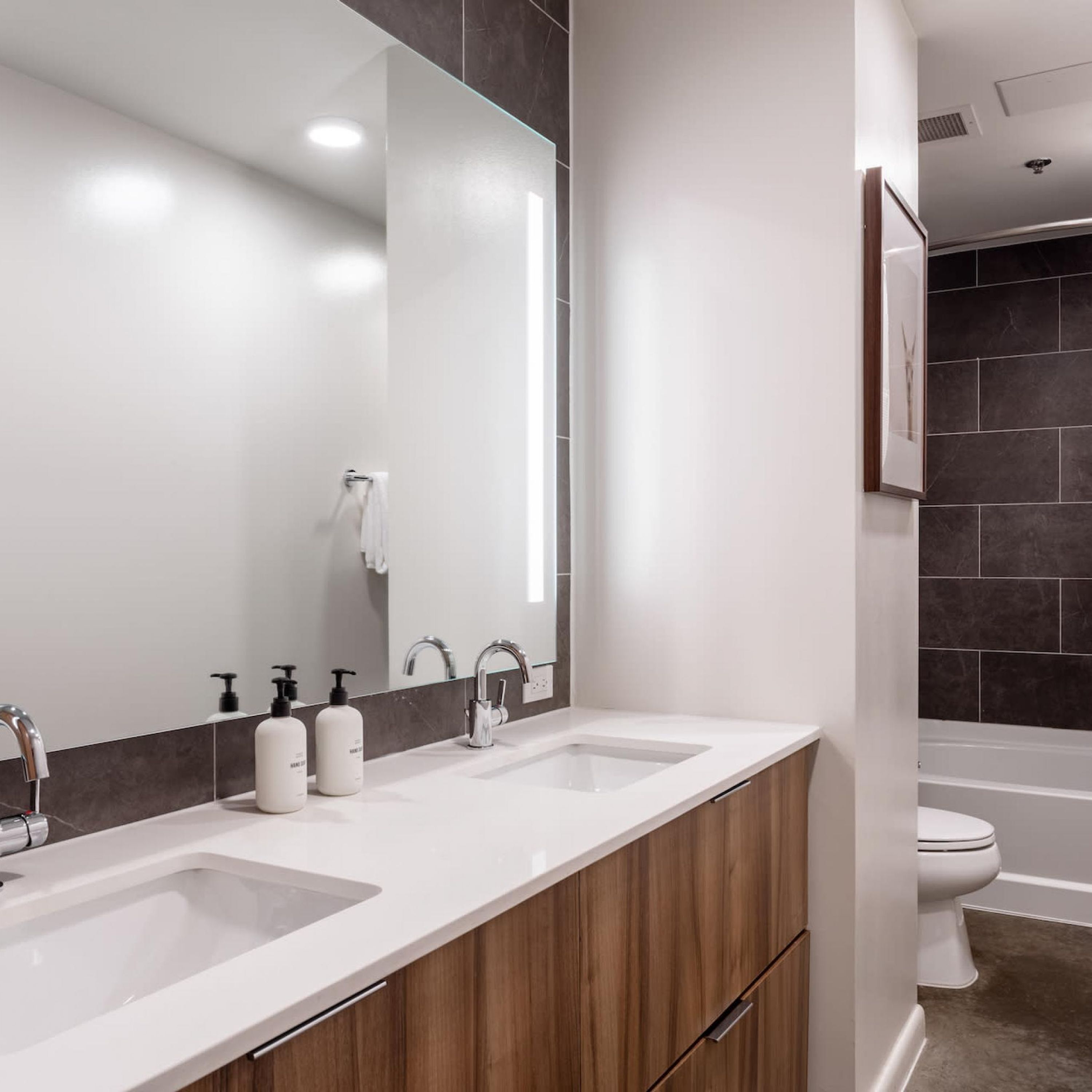 A modern bathroom with two sinks, a large mirror, and a toilet.