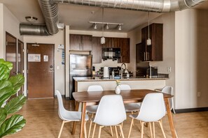 Une cuisine moderne dotée d’appareils électroménagers en acier inoxydable, une table à manger en bois avec des chaises blanches et une grande plante verte.