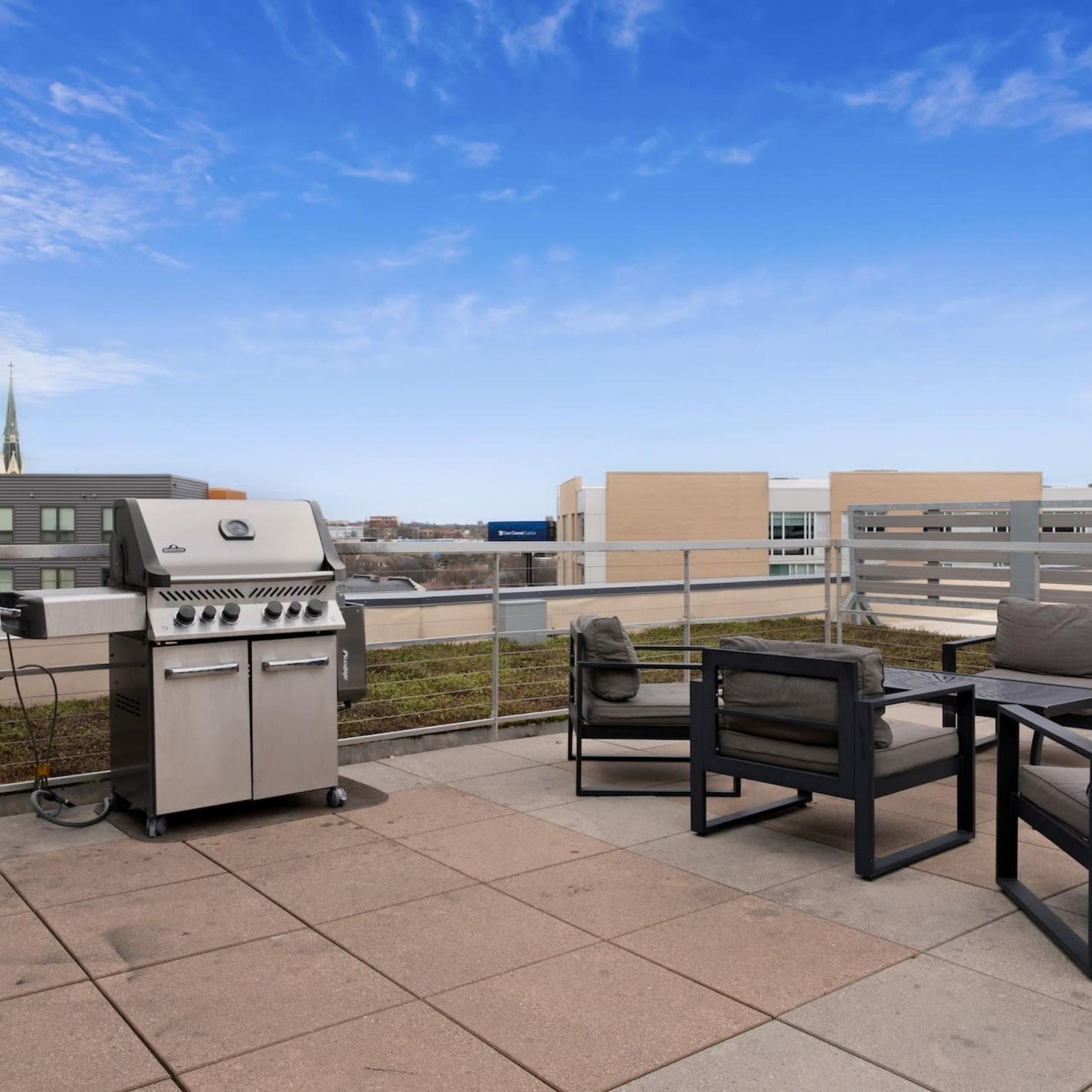 Een terras buiten met een barbecue, zitplaatsen en uitzicht op gebouwen op de achtergrond.