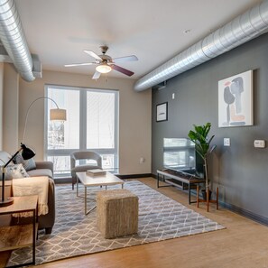 Un salon moderne doté d’un ventilateur de plafond, de grandes fenêtres, d’un téléviseur à écran plat et d’une plante en pot.