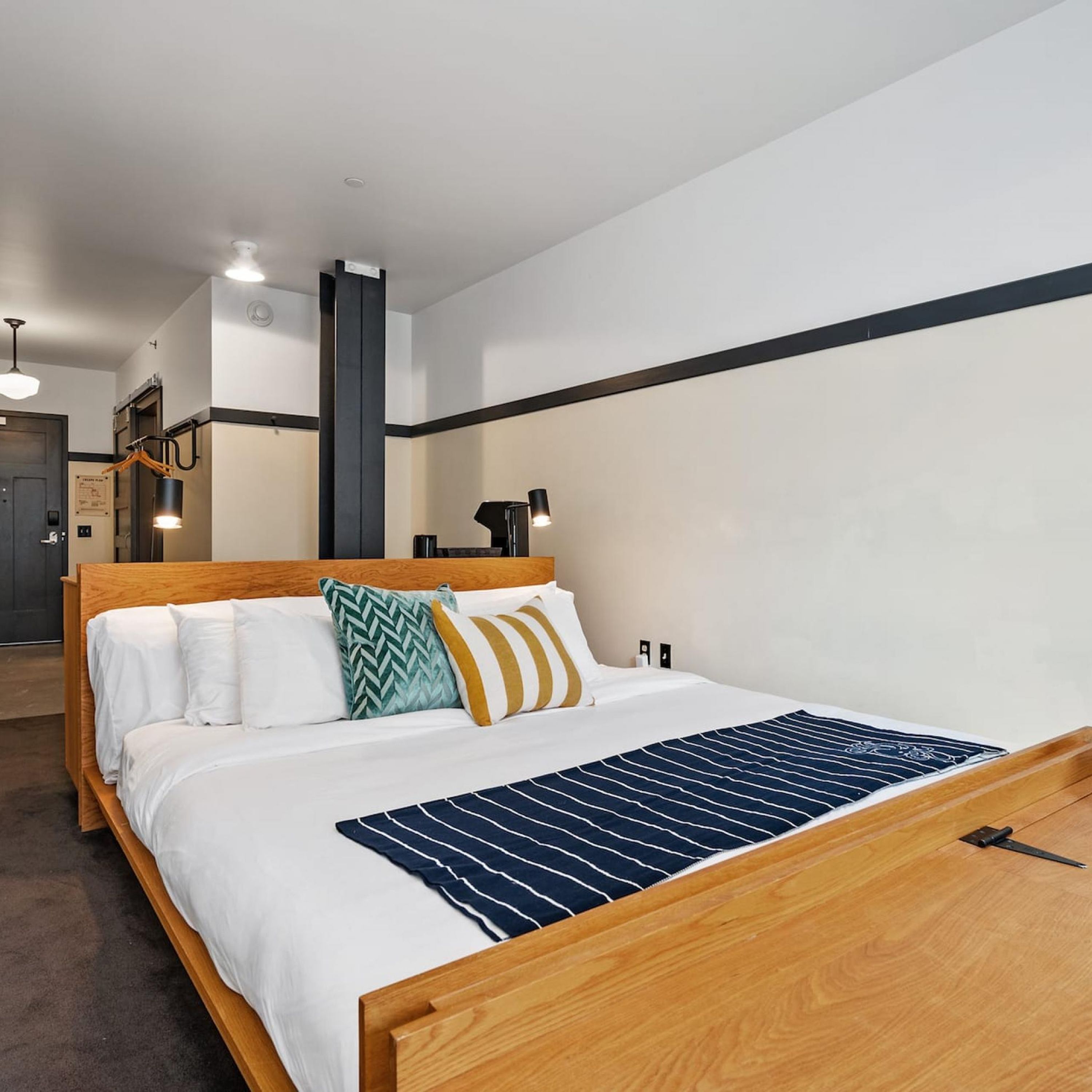 A hotel room with a wooden bed, white bedding, a striped throw, and a black headboard.