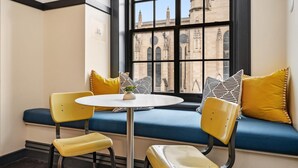 A corner seating area with a blue cushioned bench, yellow chairs, and a small round table with a plant.