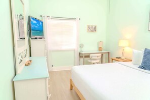 A hotel room with a bed, a desk with a chair, a small table with a lamp, a window with blinds, and a television on a stand. - Golf Colony at Deerfield 19-D (Myrtle Beach)