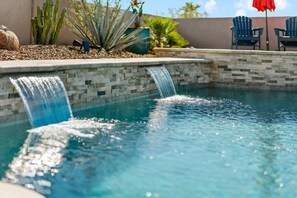 Una piscina con una cascata, circondata da un muro in pietra e diverse piante.