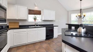 A modern kitchen with white cabinets, a black countertop, and a built-in oven. - Enjoy a nice home with a beautiful garden.   (Fort worth)