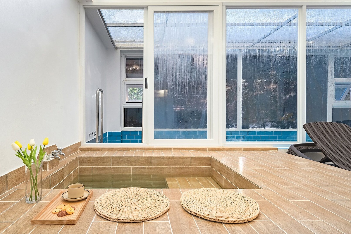 A modern bathroom with a glass-enclosed shower, a bathtub, and a seating area with a chair and a table.