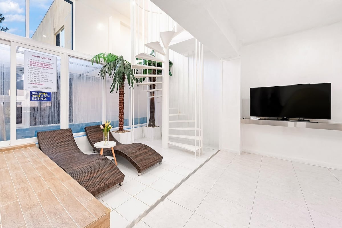 A modern living room with a large window, a flat-screen TV, and a seating area with wicker furniture.