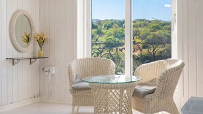 A balcony with wicker chairs, a glass table, a white wicker side table, a mirror, and a vase with flowers.