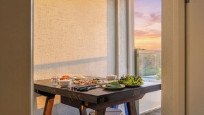 Et spisebord med mad og drikkevarer, placeret ved et vindue med udsigt til en solnedgang.