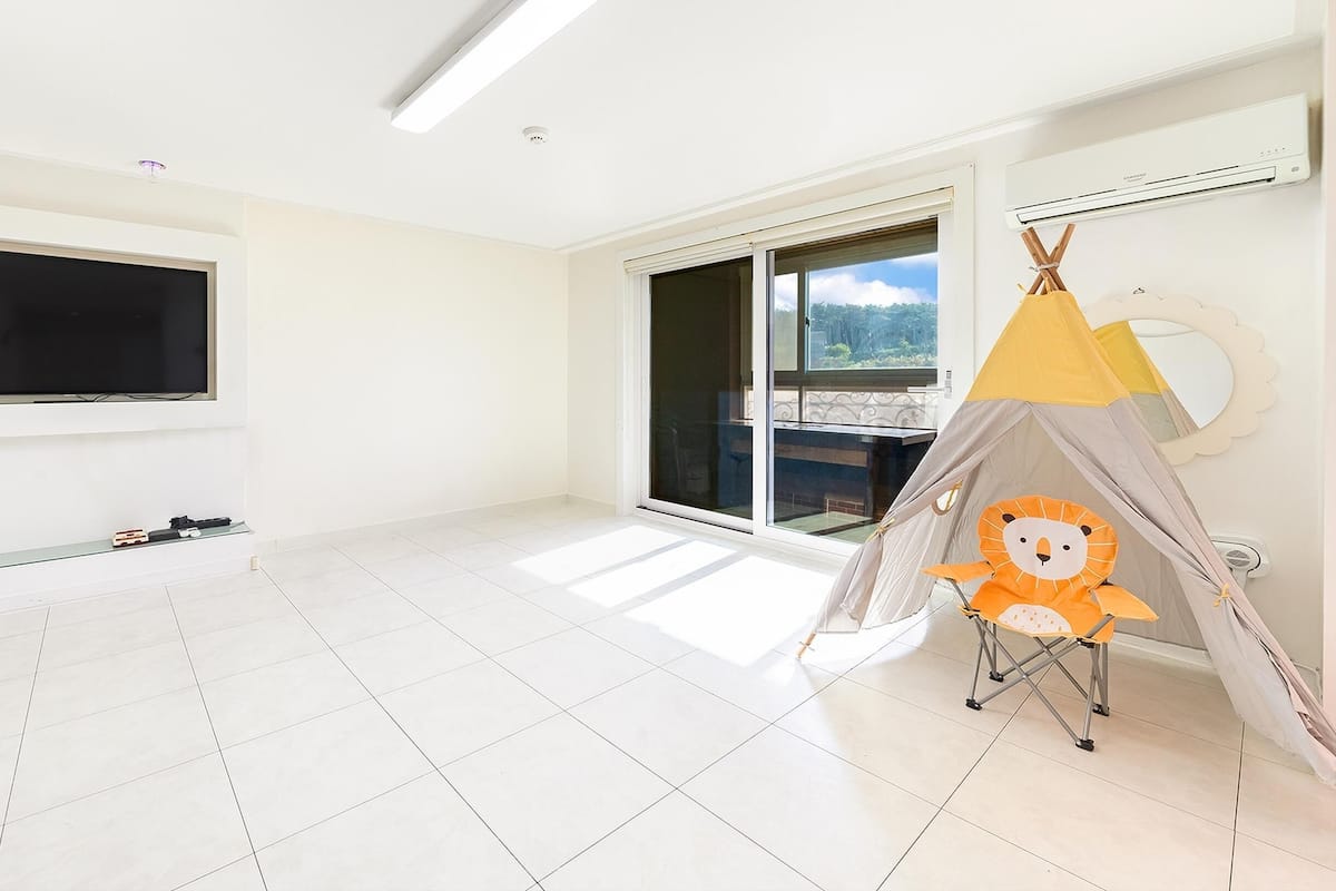 A spacious room with a large TV, a sliding glass door to a balcony, and a children's play tent.