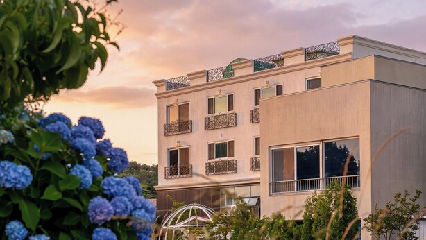 A multi-story building with balconies, large windows, and a garden with blue flowers. - Gyeongju Jullietapoolvilla&kidspension (Gyeongju)