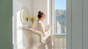 A room with a large window, a wicker chair, a glass table, and a mirror.