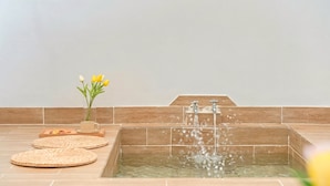 A spa area with a rectangular hot tub, a wooden bench, and a vase with yellow flowers. - Gyeongju Jullietapoolvilla&kidspension (Gyeongju)