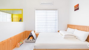 A bedroom with a bed, a window with blinds, a wall-mounted air conditioner, and a small shelf with a toy. - Gyeongju Jullietapoolvilla&kidspension (Gyeongju)