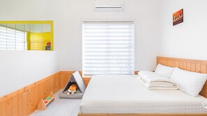A bedroom with a bed, a window with blinds, a wall-mounted air conditioner, and a small shelf with a toy.