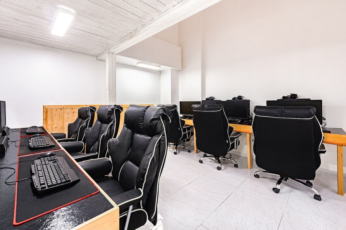 A modern office space with multiple workstations, ergonomic chairs, and a long table with computers and keyboards.